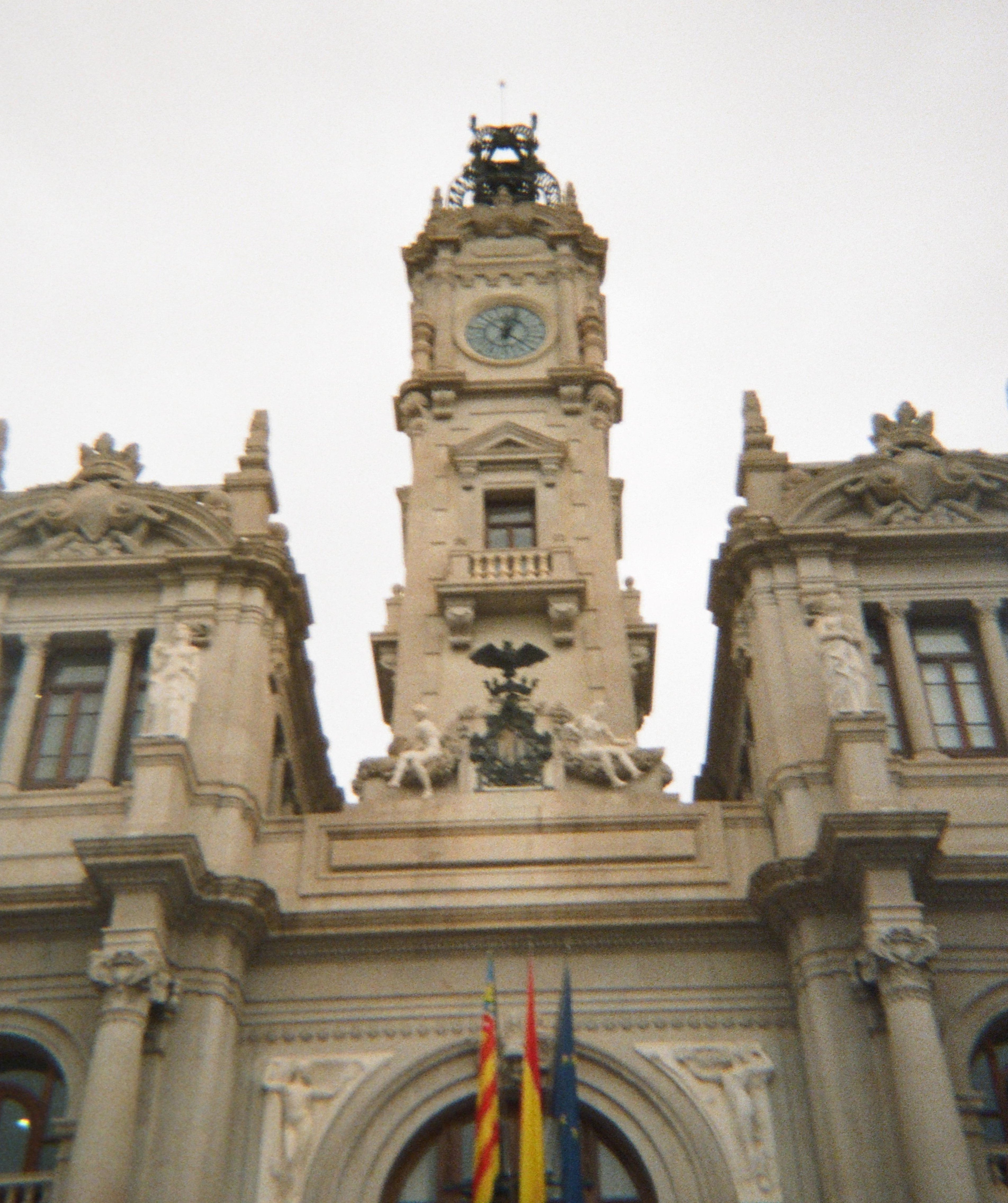 Blurred image of a clock tower on a building facade with flags.