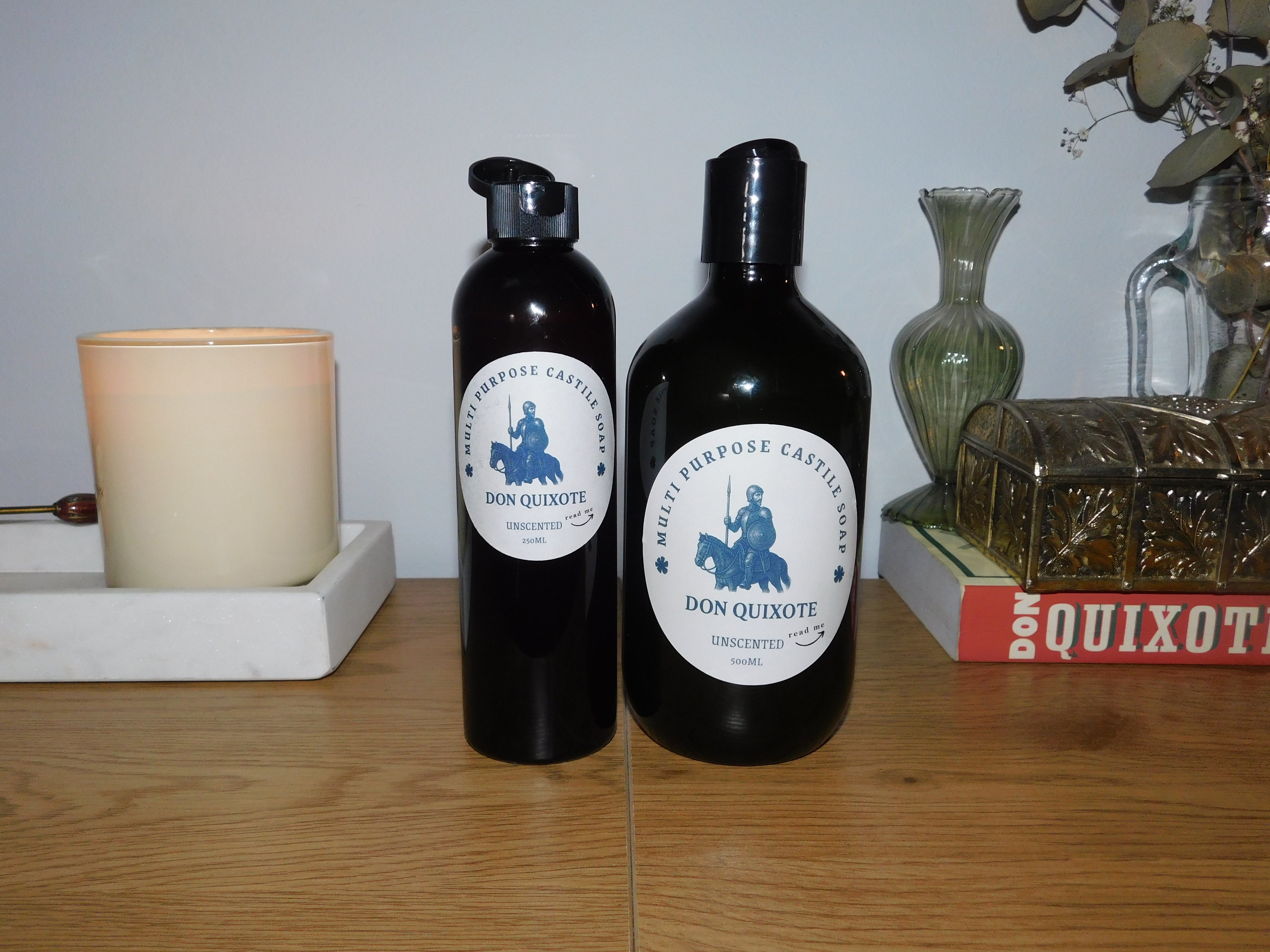 Two black bottles with white labels on a wooden surface, with decorative items in the background.